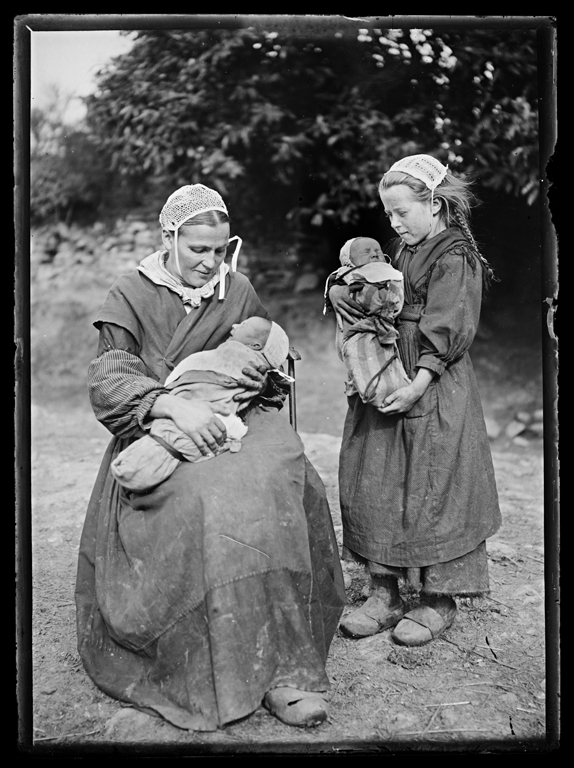 Photographie d'une paysanne et d'une fillette tenant deux bébés emmaillotés.